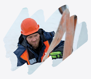 Arbeider med oransje hjelm og synlig vernevest håndterer lastestropper under vinterforhold, iført grønne arbeidshansker for sikkerhet og grep.