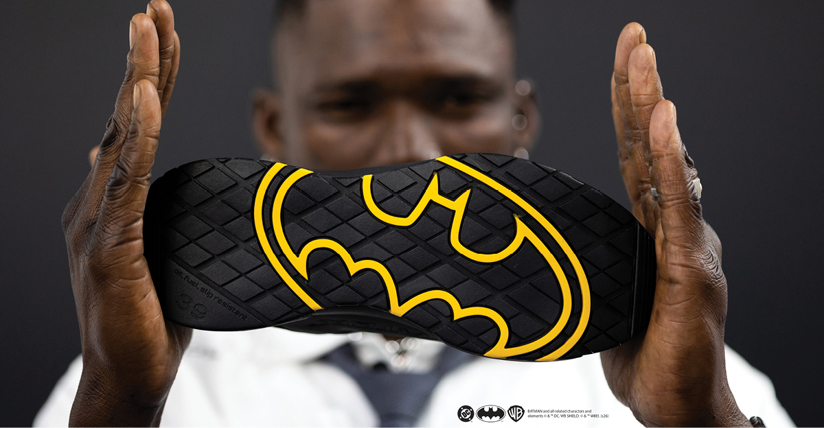 Miljøbilde av en person som holder verneskoen Bat.One med sålen mot kamera - symbolet for Batman i gult som en del av den svarte sålen. Verneskoen er en nyhet som kommer i Limited Edition og selges kun hos Ahlsell, kampanje i en begrenset periode.